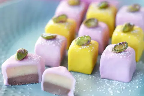 Små, färgglada marsipanbitar med pistage, perfekta för påskgodis recept. En av dem är uppskuren och visar lager av choklad och mandelmassa.