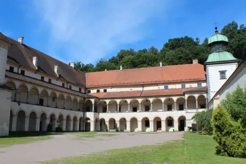 Dziedziniec zamku w Suchej Beskidzkiej z arkadowymi krużgankami i zieloną wieżą.