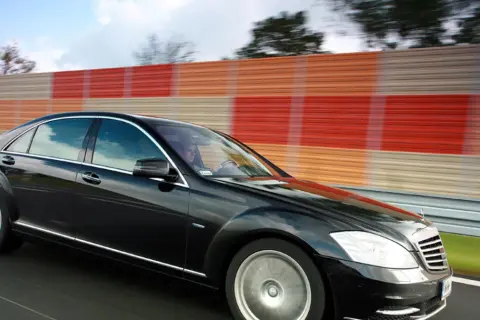 Czarny Mercedes S400d pędzi autostradą obok kolorowego ekranu dźwiękochłonnego.