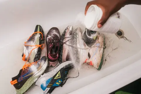 Mani versano polvere da un contenitore su diverse scarpe da ginnastica in una vasca da bagno, un modo per disinfettare scarpe usate.