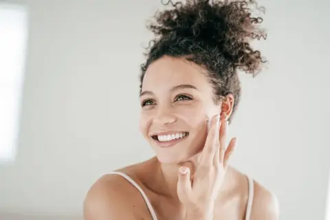 Mujer sonriente aplicándose crema, un paso esencial para el cuidado de piel grasa.