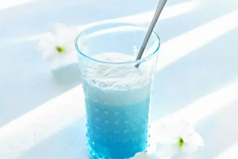 Ein erfrischender Blue Curacao Cocktail in einem strukturierten Glas, garniert mit weißen Blüten.