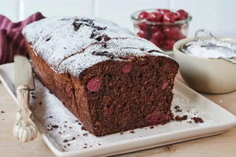 Saftiger schoko kirsch kuchen, bestäubt mit Puderzucker. Daneben eine Schale mit Kirschen und ein Sieb.
