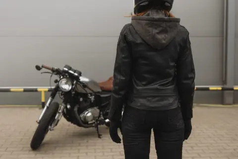 Kobieta w skórzanej kurtce motocyklowej i kasku stoi obok motocykla.
