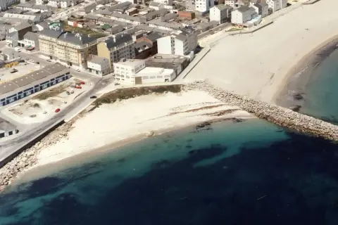 Vista aérea de la playa Penoural en Burela, con edificios urbanos y el mar azul turquesa.