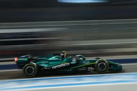 Un coche Aston Martin Honda verde compite a gran velocidad en una pista nocturna, con las luces y el fondo difuminados por el movimiento.