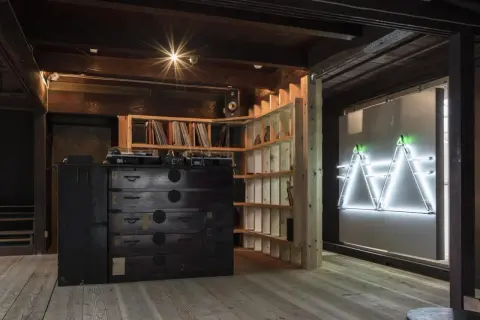 Theaster Gates studio: A DJ setup sits atop a dark wooden chest of drawers, surrounded by shelves of records and a striking neon art installation.