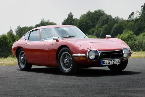 Klasyczny, czerwony Toyota 2000GT, jeden z najbardziej ikonicznych japońskich samochodów sportowych, prezentuje swoje eleganckie linie na tle zieleni.