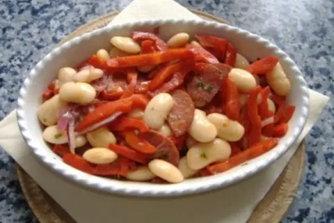 Ein herzhafter spanischer Bohnensalat mit weißen Bohnen, roten Paprikastreifen und Chorizo in einer weißen Schüssel.
