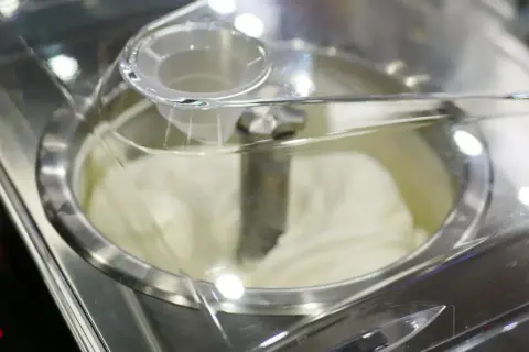 Cremiges Sahneeis wird in einer Eismaschine zubereitet. Der Rührarm dreht sich, um die perfekte Konsistenz zu erzeugen.