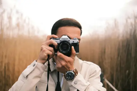 Man with a Canon AE-1, a classic choice for the best film camera for street photography, captures the moment amidst tall grasses.