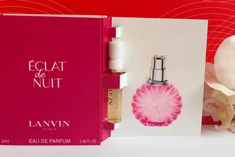 Próbka perfum Lanvin Éclat de Nuit, z buteleczką i kartonikiem z wizerunkiem flakonu, na tle czerwonych wzorów i białych kwiatów.