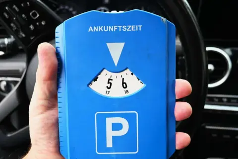Blaue Parkscheibe mit "Ankunftszeit" und "P"-Symbol. Beachten Sie die Parkuhr Regeln für die korrekte Einstellung der Ankunftszeit.