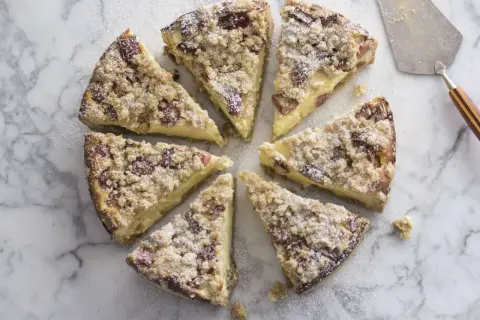 Süßer Rhabarber Schmand Kuchen, in Stücke geschnitten, mit Puderzucker bestäubt, auf Marmorplatte.