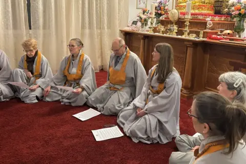 Menschen in buddhistischen Roben sitzen auf einem roten Teppich und lesen buddhistische Mantratexte.