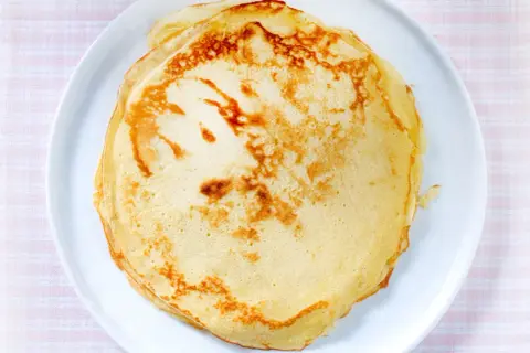 Ein Stapel goldbrauner, veganer Pfannkuchen liegt auf einem weißen Teller. Perfekt für ein leichtes Frühstück.