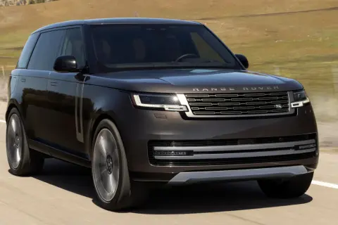 Elegancki, ciemnobrązowy Range Rover 2025 pędzi po pustej drodze, otoczony suchymi, pagórkowatymi krajobrazami.