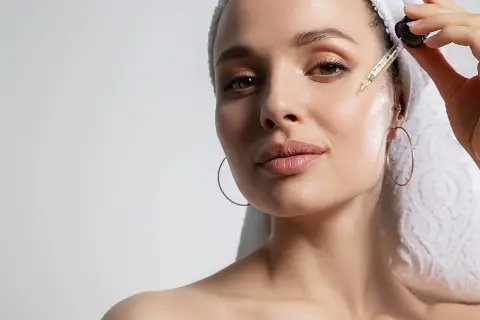 Mujer con toalla en la cabeza aplica gotas de sérum con péptidos para la cara, buscando una piel radiante y rejuvenecida.