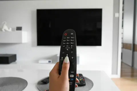 Dłoń trzymająca pilot do telewizora, gotowa do włączenia obrazu w rozdzielczości 4k.