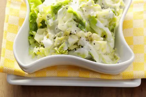 Cremiger Weißkohlsalat, ein einfaches wirsing rezept, serviert in einer weißen Schüssel auf gelb-weiß karierter Serviette.