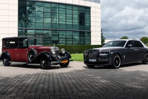 Dwa Rolls-Royce'y Phantom: zabytkowy czerwono-czarny i nowoczesny grafitowo-biały, stojące przed budynkiem.