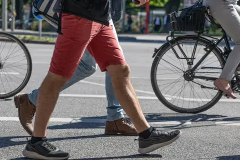 Ludzie przechodzą przez pasy, jeden na rowerze, drugi pieszo. Czy jazda na rowerze odchudza brzuch? To pytanie zadaje sobie wielu.