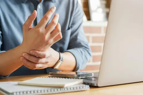 Uomo con male ai polsi mentre lavora al computer. Dolore al polso da uso prolungato del mouse e tastiera.