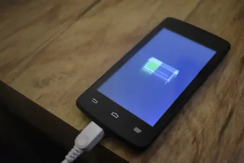 Smartfon podłączony do ładowania, na ekranie ikona baterii. Dowiedz się, jak włączyć szybkie ładowanie, by mieć więcej energii!