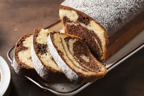 Pyszne ciasto zebra w keksówce, posypane cukrem pudrem, z kilkoma pokrojonymi kawałkami.