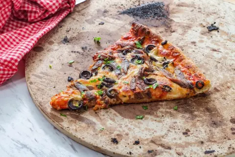 Kawałek pizzy z anchois i oliwkami na kamieniu. Dowiedz się, jak wyczyścić kamień do pizzy, by był jak nowy.