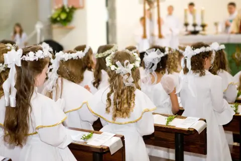 Dziewczynki w bieli, z wiankami na głowach, czekają na uroczystość. Krótkie życzenia na komunię dla nich.