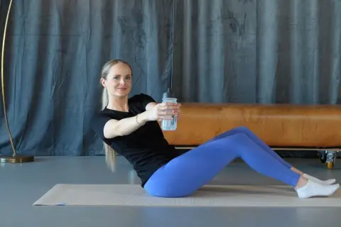 Frau macht isometrisches Training auf einer Matte, hält eine Wasserflasche und dreht den Oberkörper.