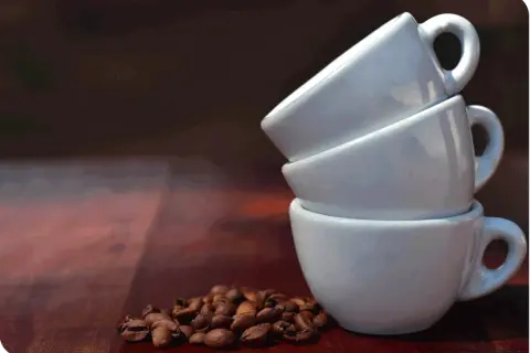 Tre tazzine bianche impilate e chicchi di caffè. Una tazzina di caffè contiene circa 60 ml.