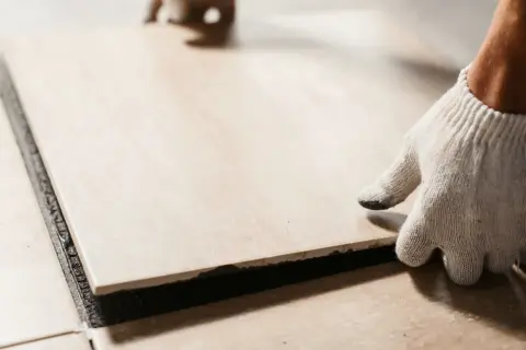 A gloved hand places a tile. Walking on tile too soon can cause shifting and unevenness.