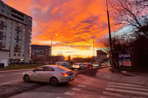 Spektakularny zachód słońca Kraków maluje niebo na pomarańczowo i różowo nad ulicą z samochodami i blokami.