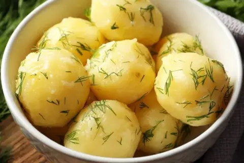 A white bowl filled with fluffy ziemniaki na parze, sprinkled with fresh dill.