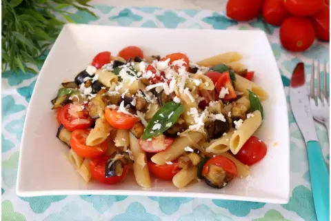 Un piatto di pasta fredda alla norma con melanzane fritte, pomodorini freschi e ricotta salata grattugiata.