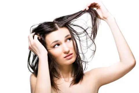 Jeune femme aux cheveux gras, se touchant la tête, l'air interrogateur. Pourquoi ces cheveux gras ?