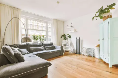 Gemütliches kleines Wohnzimmer einrichten mit großem Ecksofa, Bogenlampe, Pflanzen und mintgrünem Schrank.