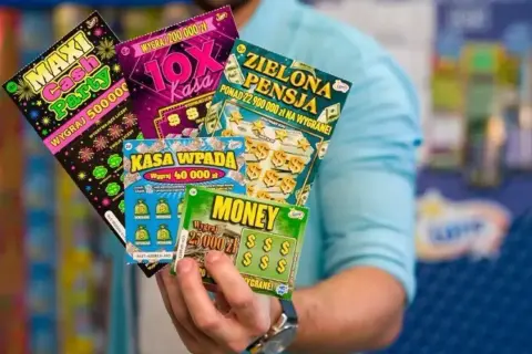 Dłoń trzyma kilka zdrapek Lotto z różnymi nazwami i kwotami wygranych.