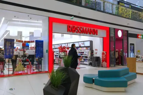 Wejście do drogerii Rossmann w centrum handlowym, z widocznymi promocjami i wystrojem świątecznym.