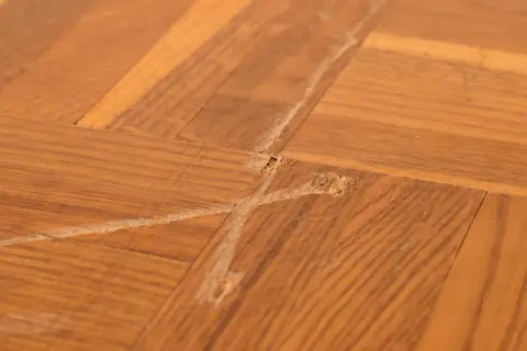 Gros plan sur un parquet en bois avec une rayure profonde et des éclats, témoignant d'une usure du temps.