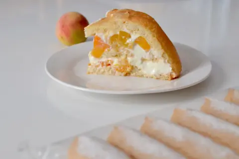 Tranche de charlotte aux fruits et fromage blanc, garnie de morceaux de pêche et de crème onctueuse. Un délice fruité et léger.