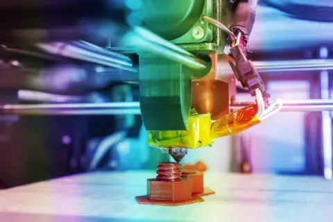 Głowica drukarki 3D drukuje brązową śrubę na platformie roboczej.