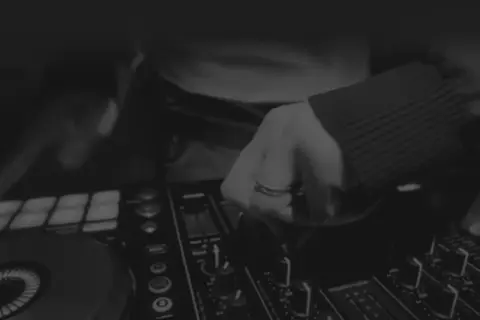 Dłoń DJ-a manipulująca pokrętłami na konsoli do miksowania muzyki.
