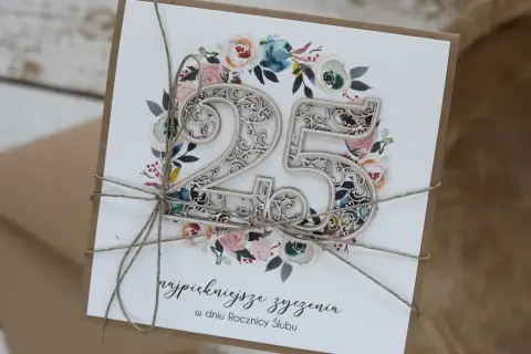Elegancka kartka z napisem "najpiękniejsze życzenia w dniu Rocznicy Ślubu" i ozdobnym numerem 25, otoczonym kwiatami.
