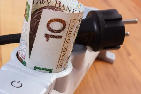 Zrolowany banknot 10 zł w gniazdku listwy zasilającej symbolizuje sposoby na oszczędzanie prądu i pieniędzy.