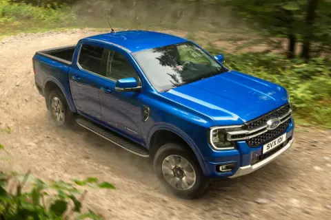 Blå Ford Ranger laddhybrid kör på en grusväg genom en skog.