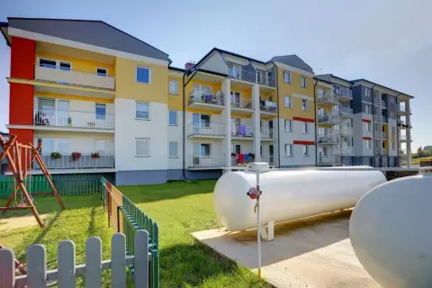 Nowoczesny blok z kolorową elewacją i balkonami. Obok plac zabaw i duże zbiorniki, które zapewniają ogrzewanie gazowe w bloku.