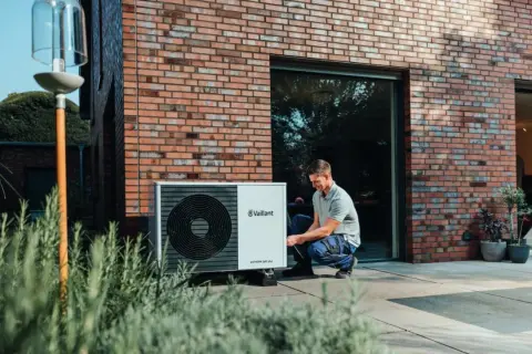 Installazione di una pompa di calore esterna: un uomo controlla l'unità posizionata vicino alla casa.